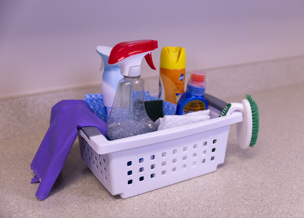 Cleaning sprays, brushes, cloths, and protective gloves in a supply basket
