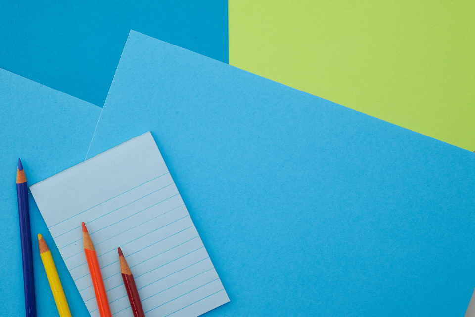 Notepad and colored pencils arranged on a blue work surface